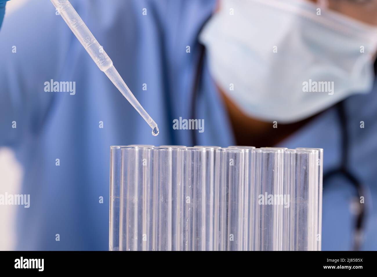 Midsection of african american mid adult female doctor wearing mask pipetting liquid in test tubes Stock Photo