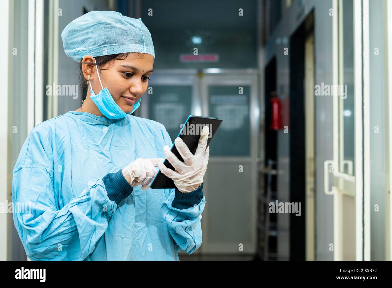 Happy surgeon busy using digital tablet at hospital corridor outside operation theater after surgery - concept of healthcare, technology and Stock Photo