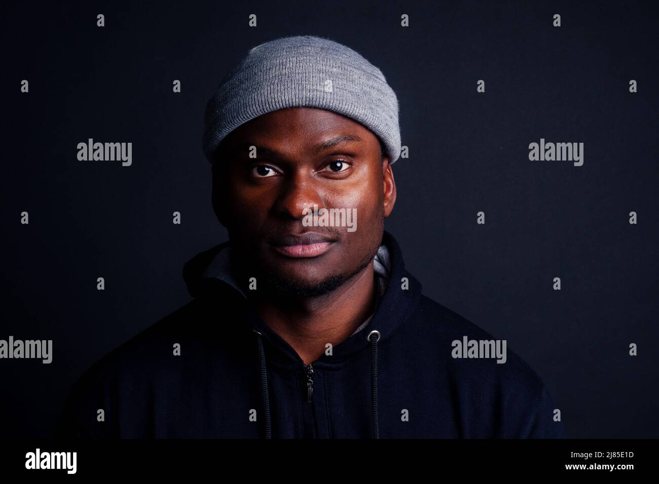 handsome afro-america male wearing gray hat and black hoody with hood serious and strong look at the camera studio shot background Stock Photo