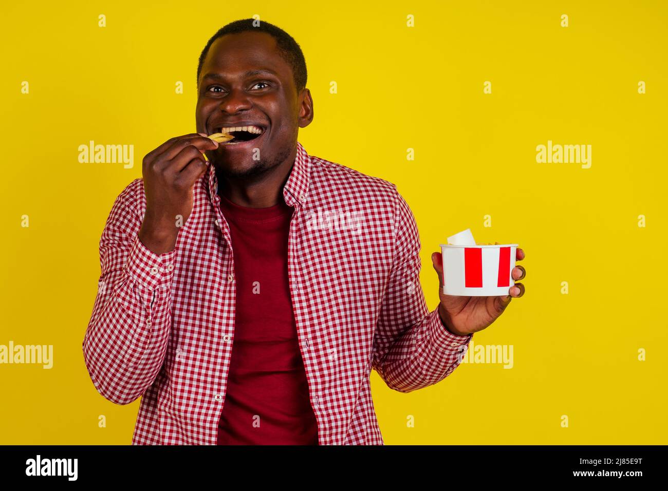 handsome latin man eating fries with appetite and enjoyment in studio yellow background Stock Photo