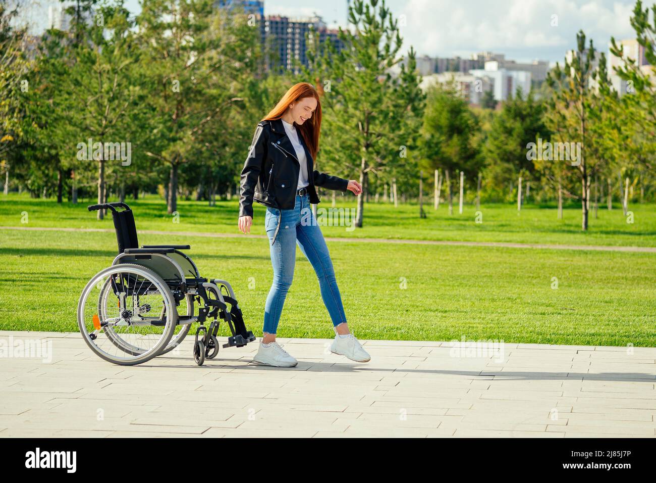 redhaired ginger woman making first steps after long recovery.she walking without her wheelchair in spring park Stock Photo