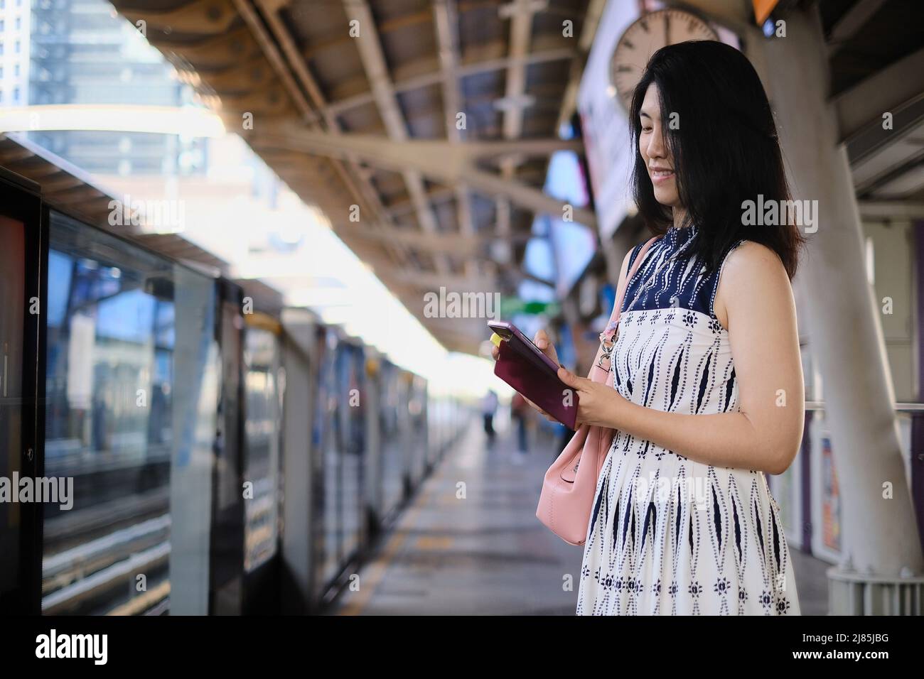 An attractive young confident Asian business woman is using her cellphone while waiting for her train at a station to go to work in the morning. Stock Photo