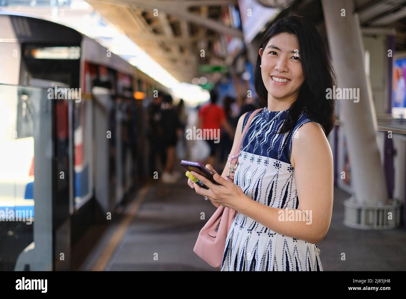 An attractive young confident Asian business woman is using her cellphone while waiting for her train at a station to go to work in the morning. Stock Photo