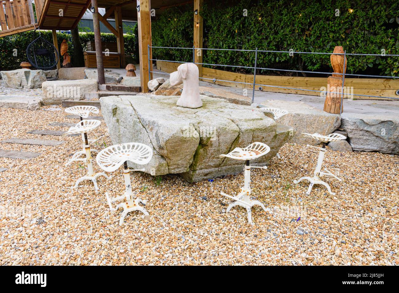 Metal bar stools around a large granite rock on an outside patio area. Stock Photo