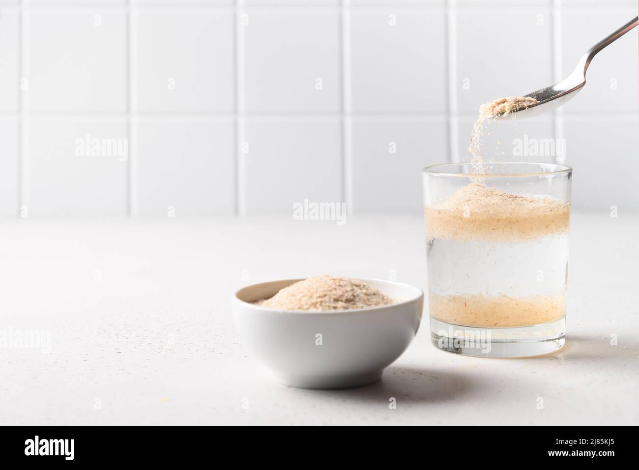 Woman adds psyllium fiber to glass of water on white background. Superfood for healthy