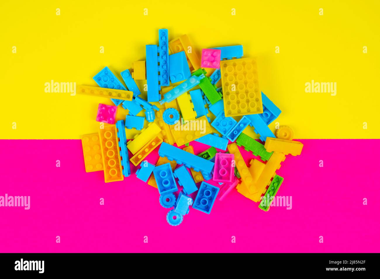 Colorful blocks toy, colored background, playing and learning concept, spilled kid toys, building blocks, yellow and pink backdrop, top view Stock Photo