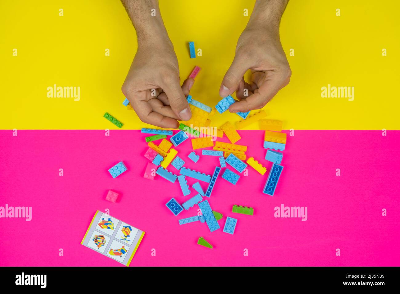 Hand playing with colorful lego blocks toy, colored background, top view, playing and learning concept, bunch of lego block, spilled kid toys Stock Photo