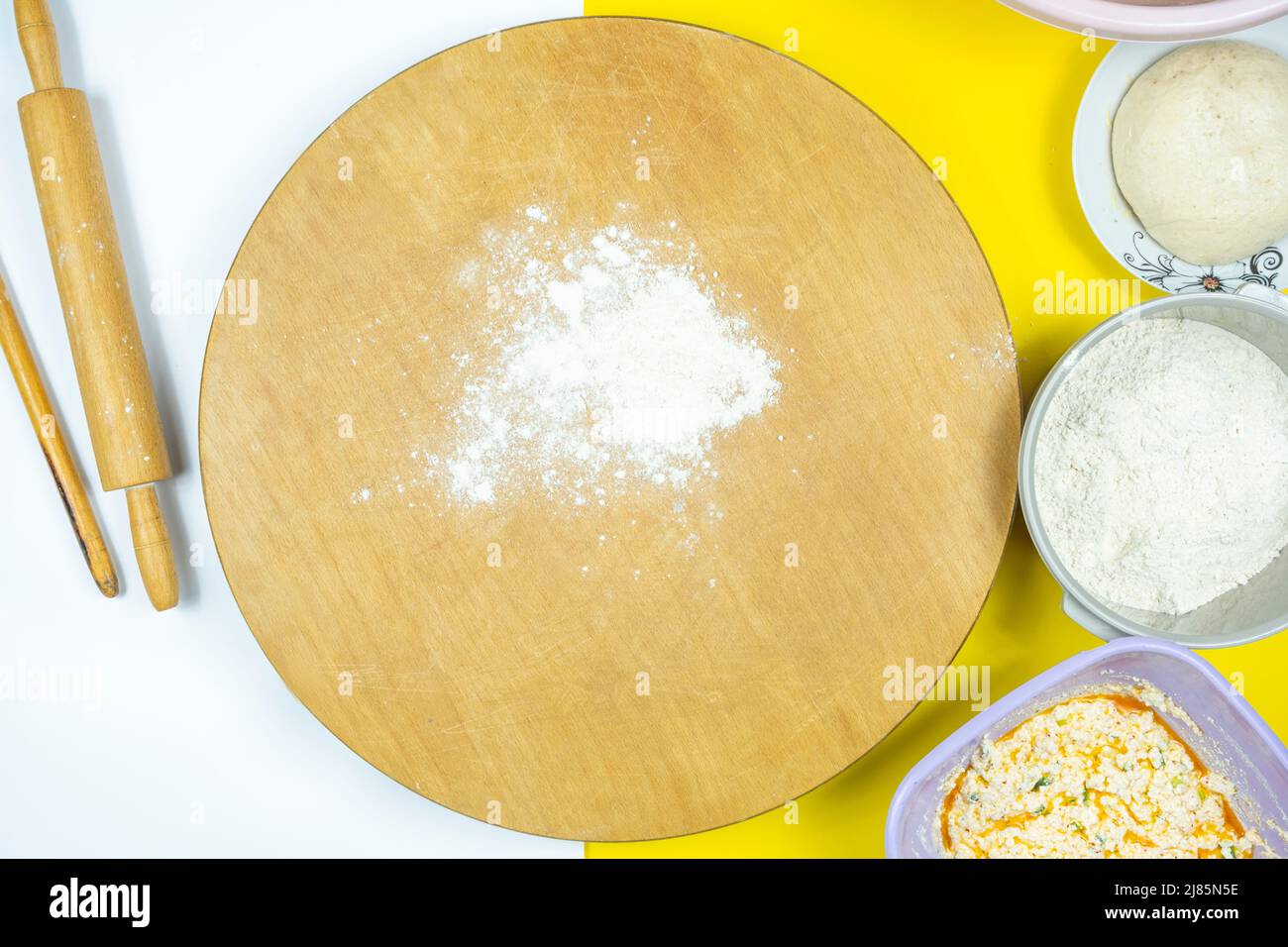 Rolling pins and traditional circle wooden board with ingredients, ingredients in the plate, top view of roller and some flour, making homemade meal Stock Photo
