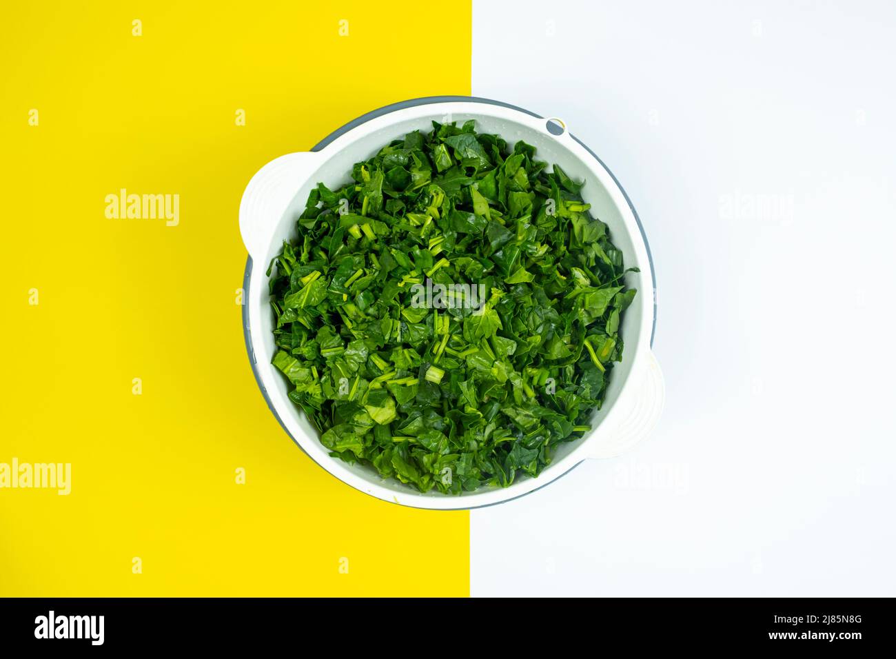 Lots of chopped spinach in white case, cooking and vegetable idea, healthy lifestyle, vegan life, yellow and white background, top view of spinach Stock Photo