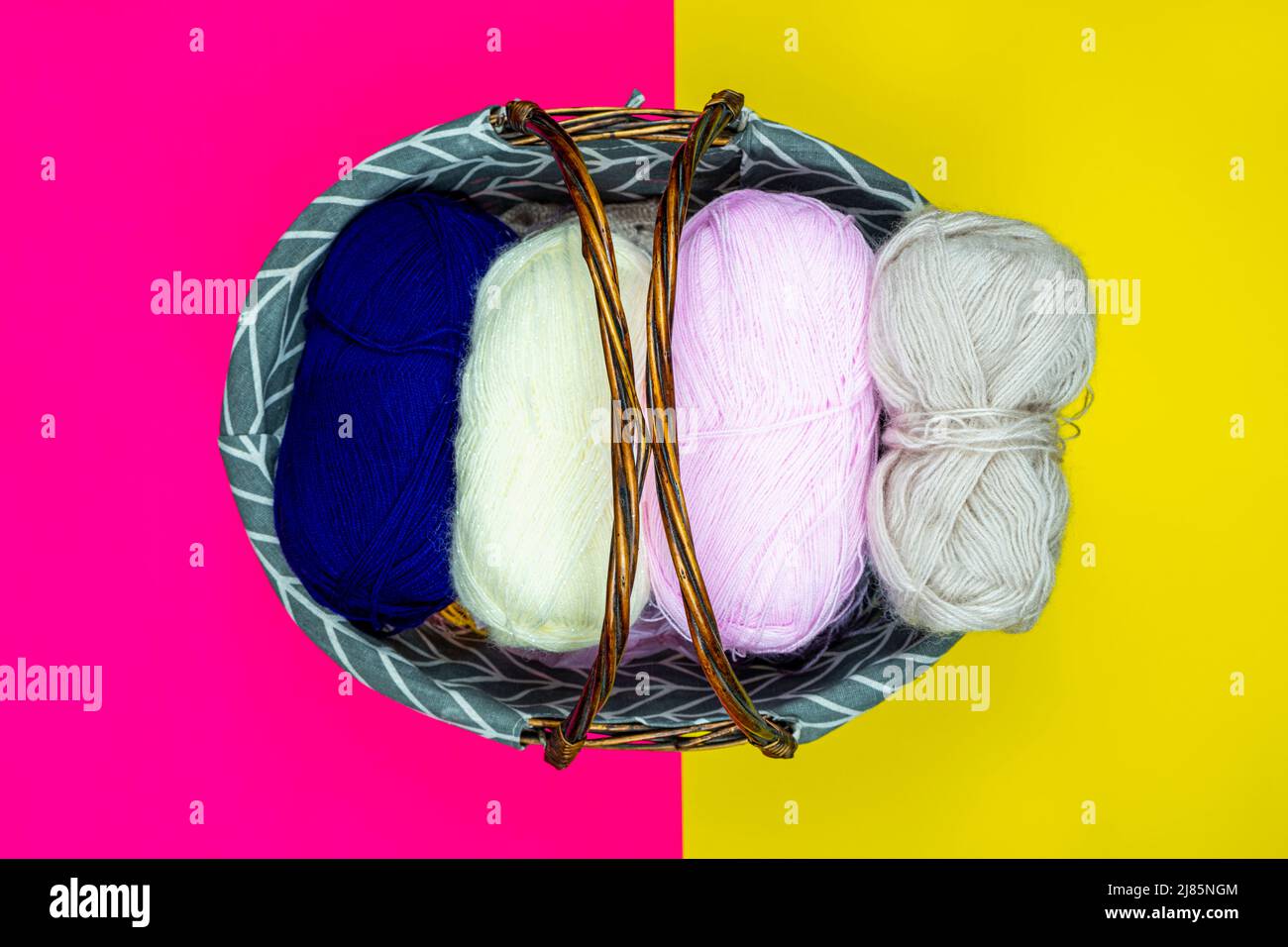 Colorful knitting threads in a wooden basket, top view, pink and yellow background, hand knitting supplies Stock Photo