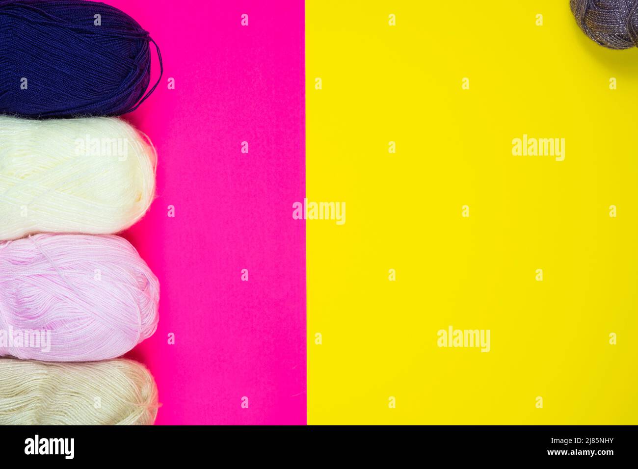 Colorful knitting thread isolated on pink and yellow background, colored background with copy space, handmade, hand knitting, top view, blue white Stock Photo