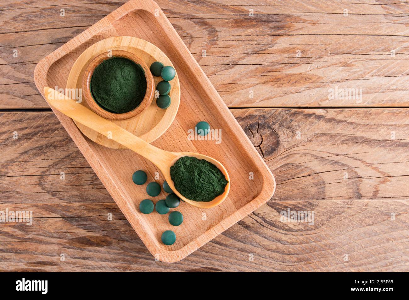top view of the wooden table with environmentally friendly dishes filled with spirulina algae powder and green tablets. food additive Stock Photo