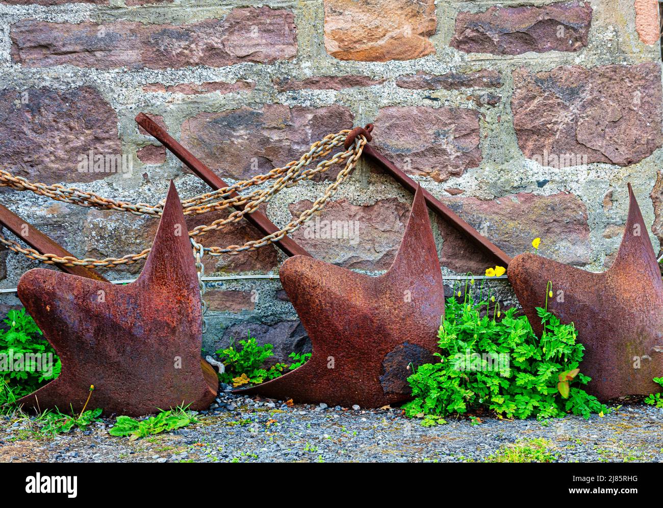 Three olld rusty metal anchors and chains outisde cottage  in the  Highland village of Plockton, Scotland Stock Photo