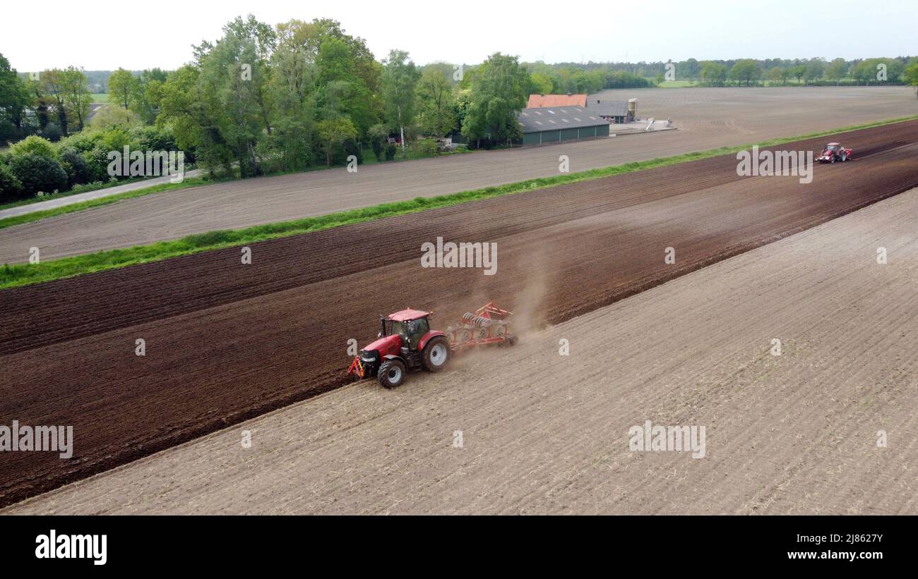A farmer is plowing his dry farmland, while another machine on the right is busy seeding potatoes. Stock Photo