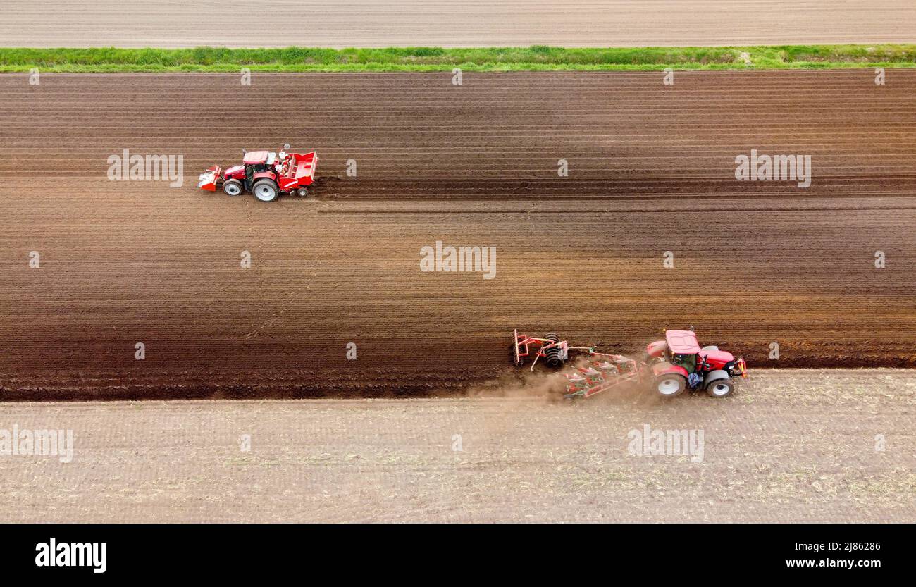A farmer is plowing his dry farmland, while another machine on the left is busy seeding potatoes. Stock Photo