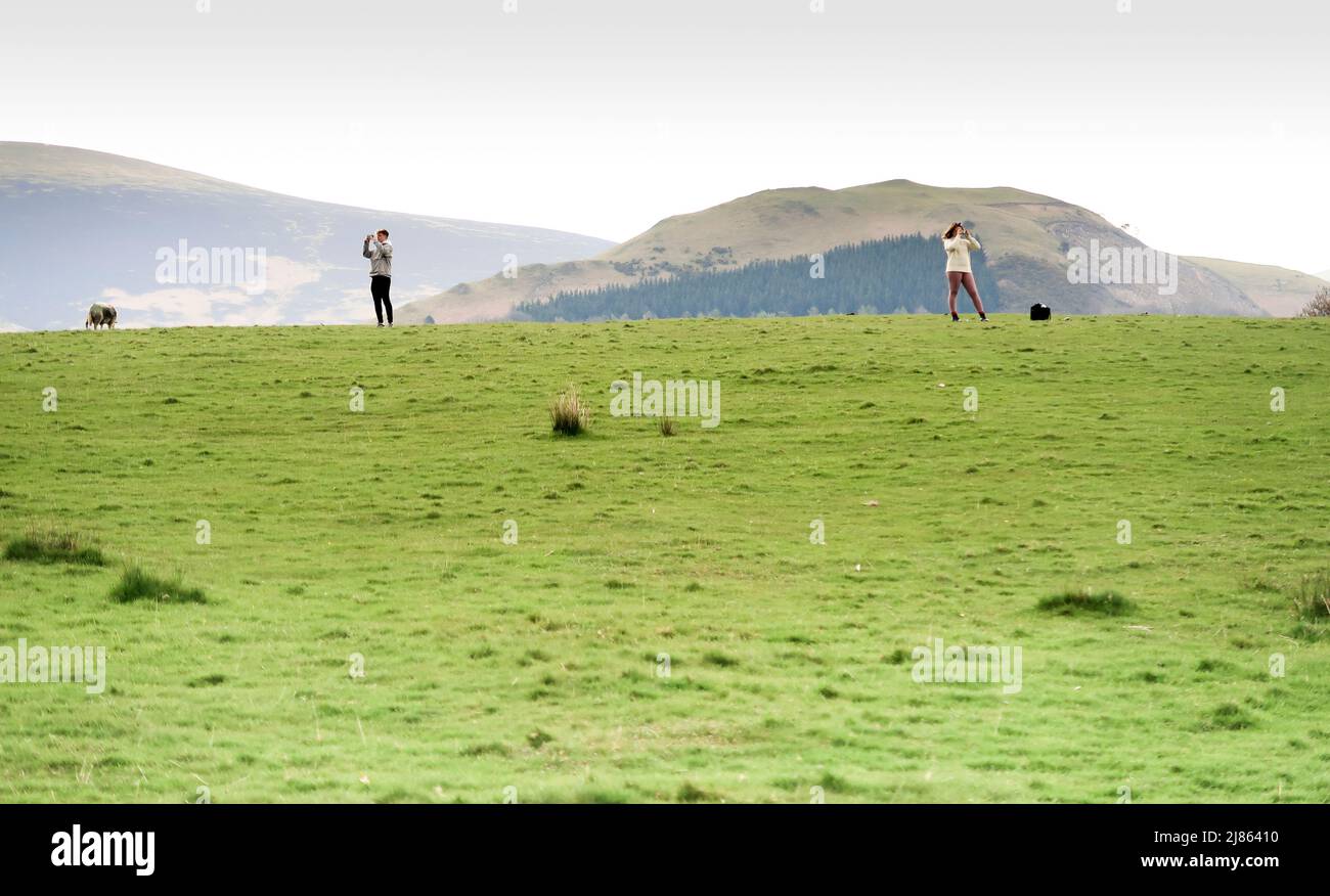 Couple taking photos on hillside in Lake District Stock Photo