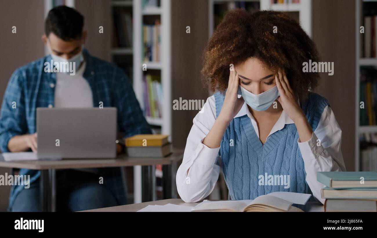 Two students in protective mask sitting in classroom at university library doing homework exam preparation young girl looking for information in book Stock Photo