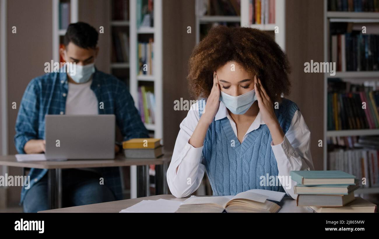 Two students in protective mask sitting in classroom at university library doing homework exam preparation young girl looking for information in book Stock Photo