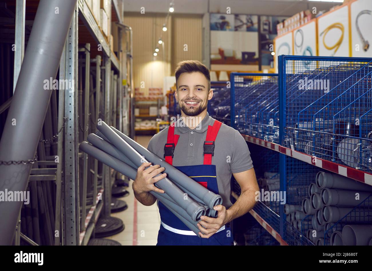 Happy salesman standing in one of the aisles, holding PVC drain pipes and smiling Stock Photo