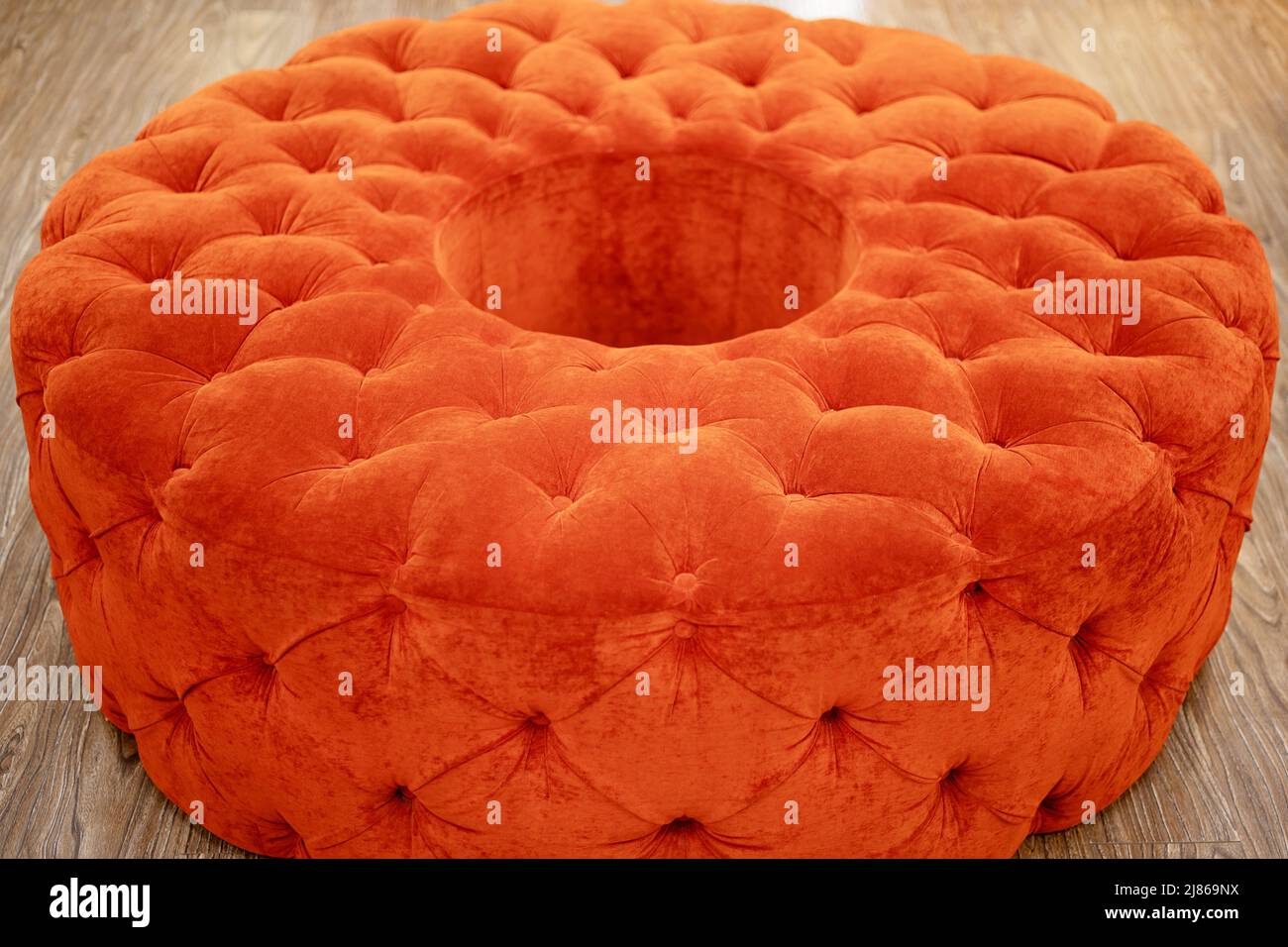 A round soft velvet pouf of red color stands on wooden floor. Classic style. Closeup photo Stock Photo