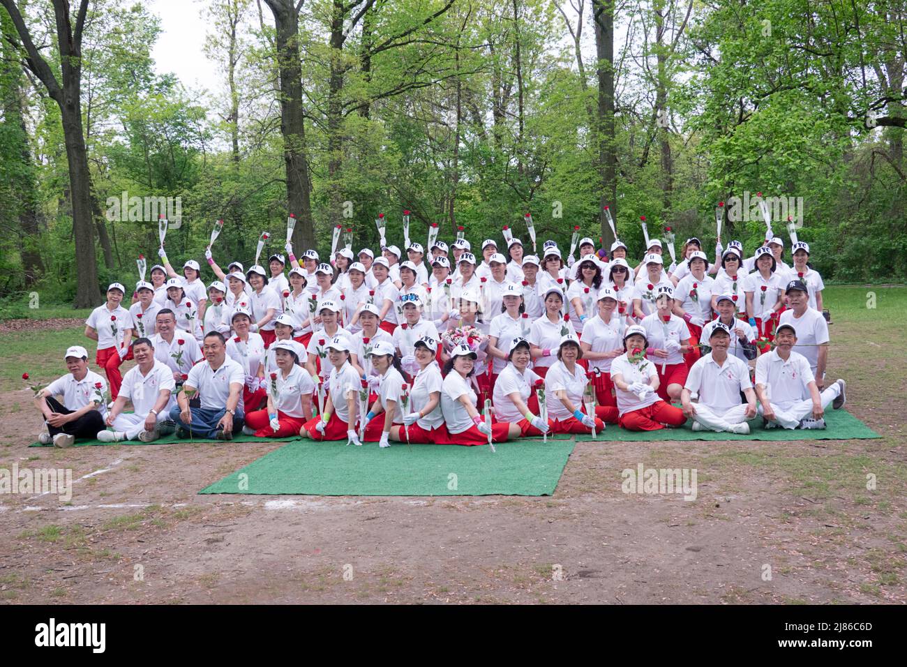 Chinese women & some men from the Kai Xin Yizhu dance troupe celebrate Mother's Day by posing for a group photo while holding roses. In a park in NYC. Stock Photo