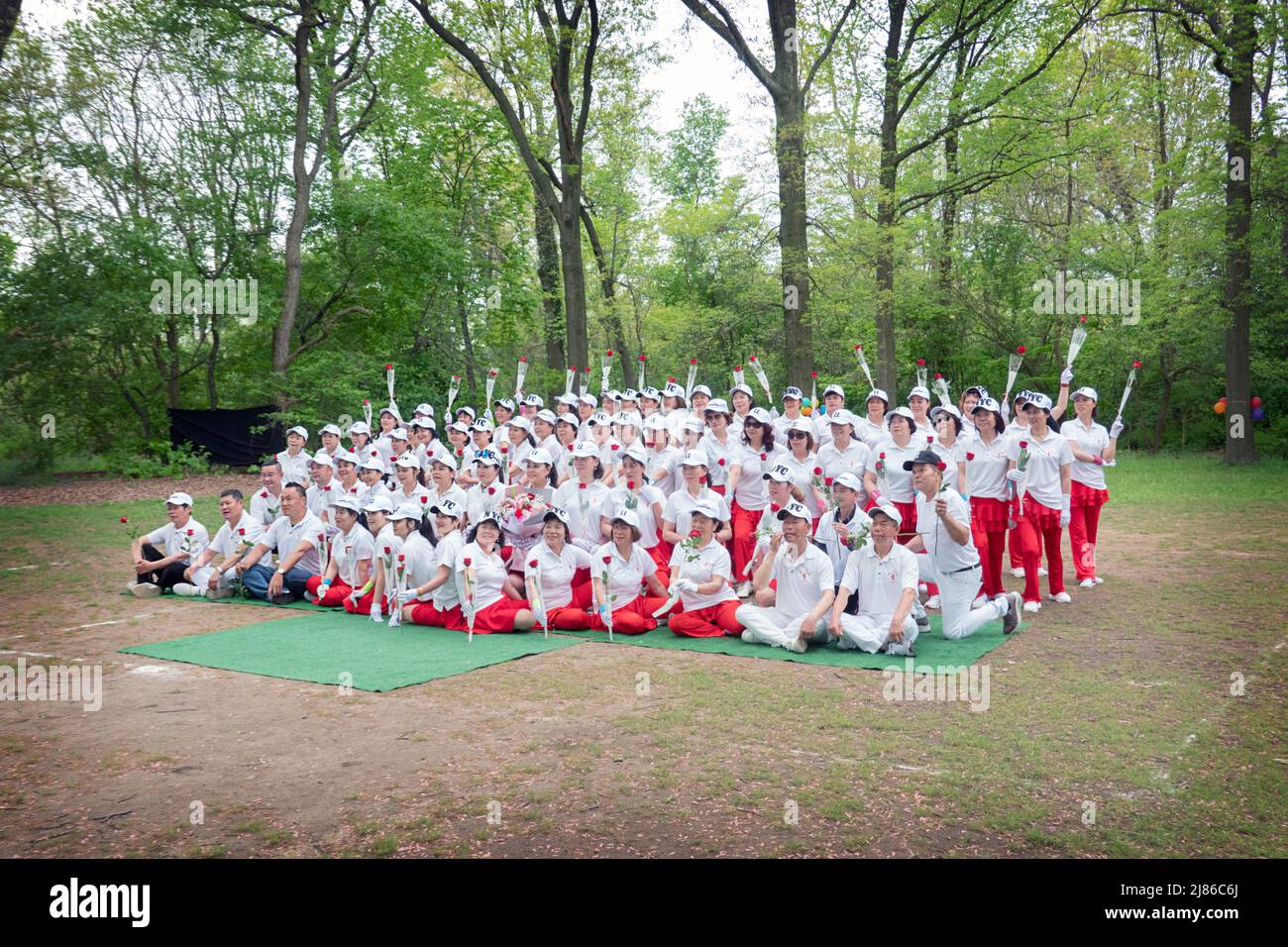 Chinese women & some men from the Kai Xin Yizhu dance troupe celebrate Mother's Day by posing for a group photo while holding roses. In a park in NYC. Stock Photo