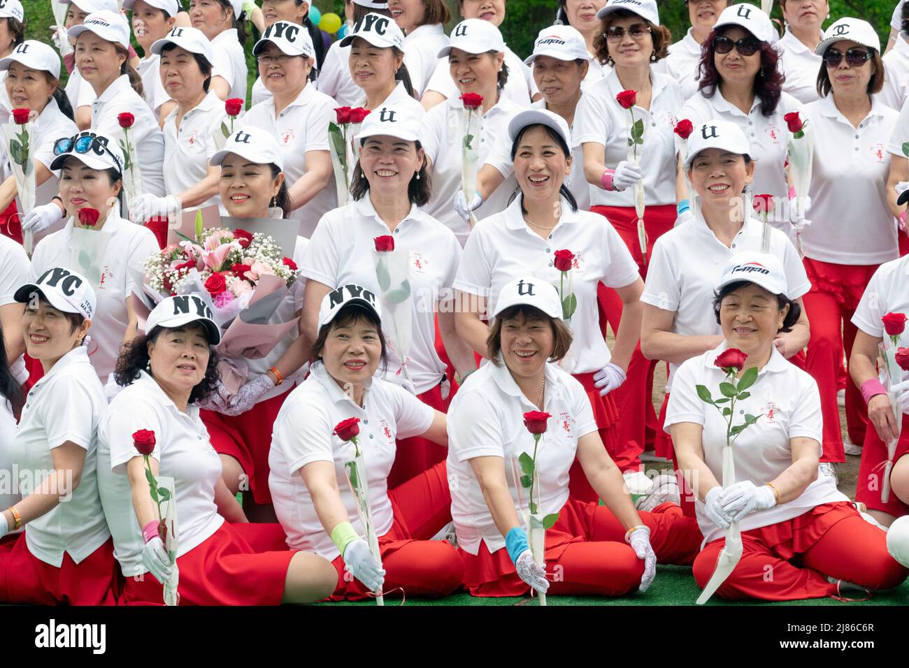 Women from Wenzhou, China in the Kai Xin Yizhu dance troupe celebrate Mother's Day by posing for a group photo while holding roses. In a park in NYC. Stock Photo