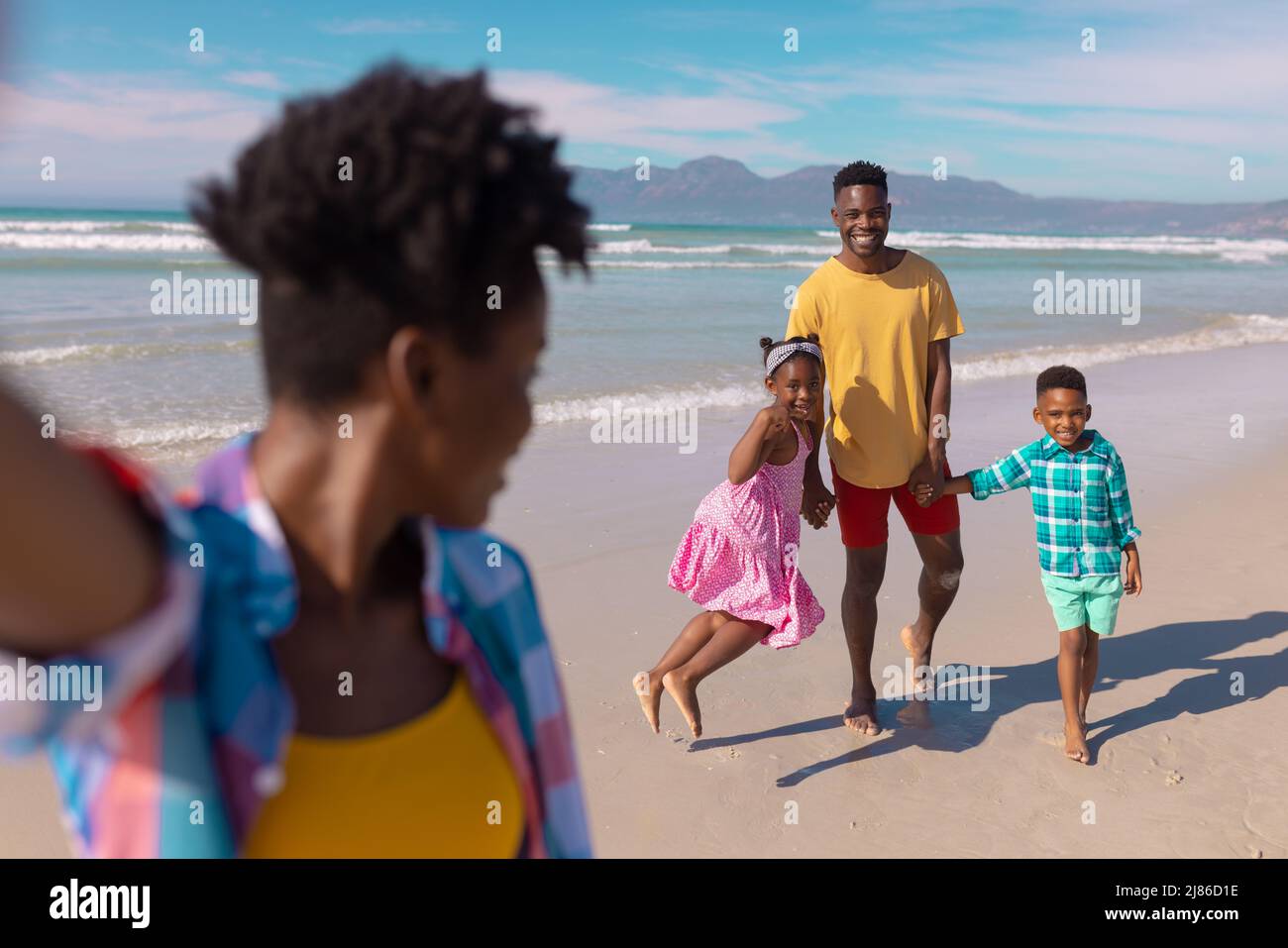 African american young woman looking at happy son, daughter and boyfriend at beach against sky Stock Photo