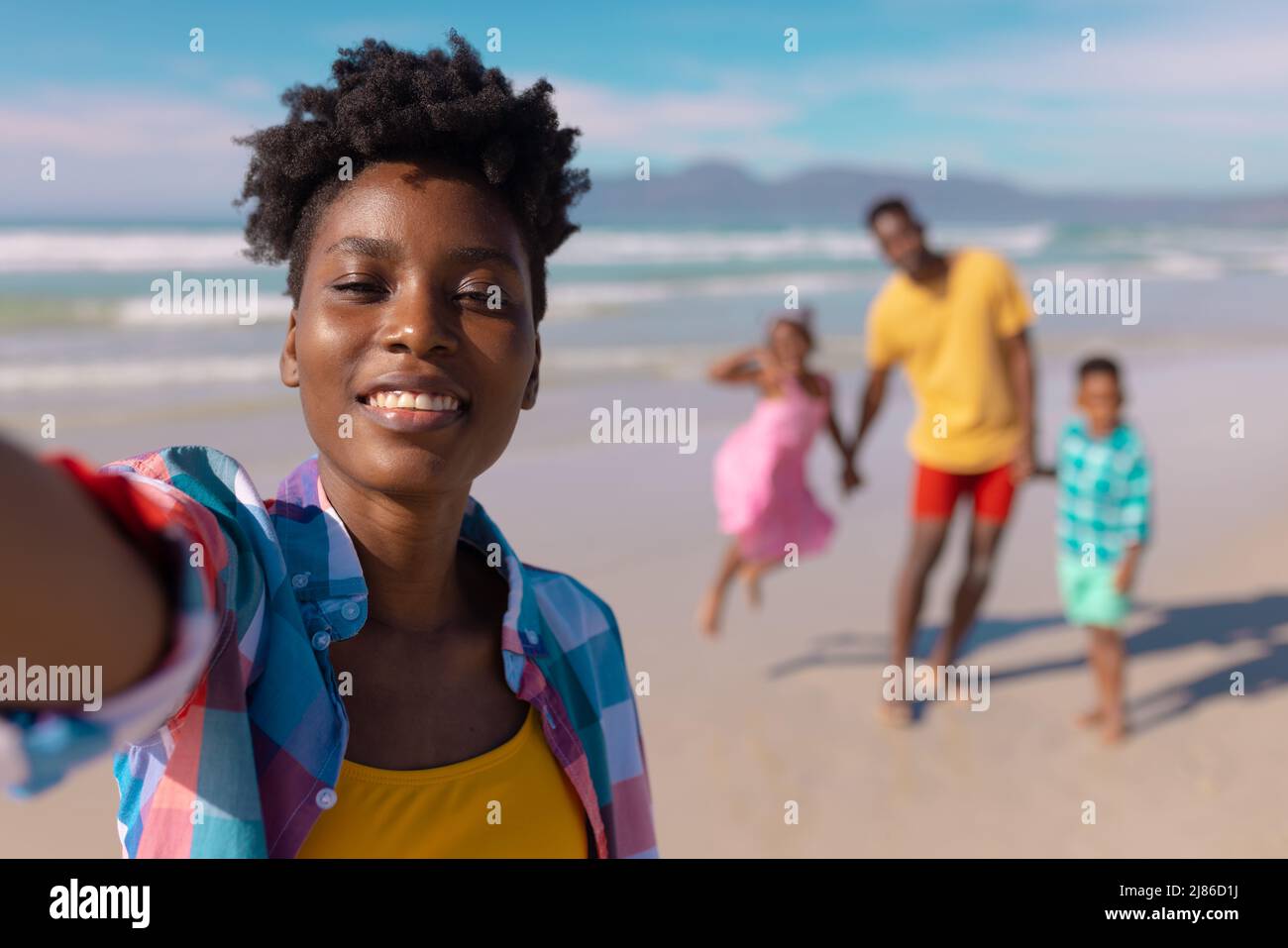 Portrait of smiling african american young woman with son, daughter and man in background at beach Stock Photo