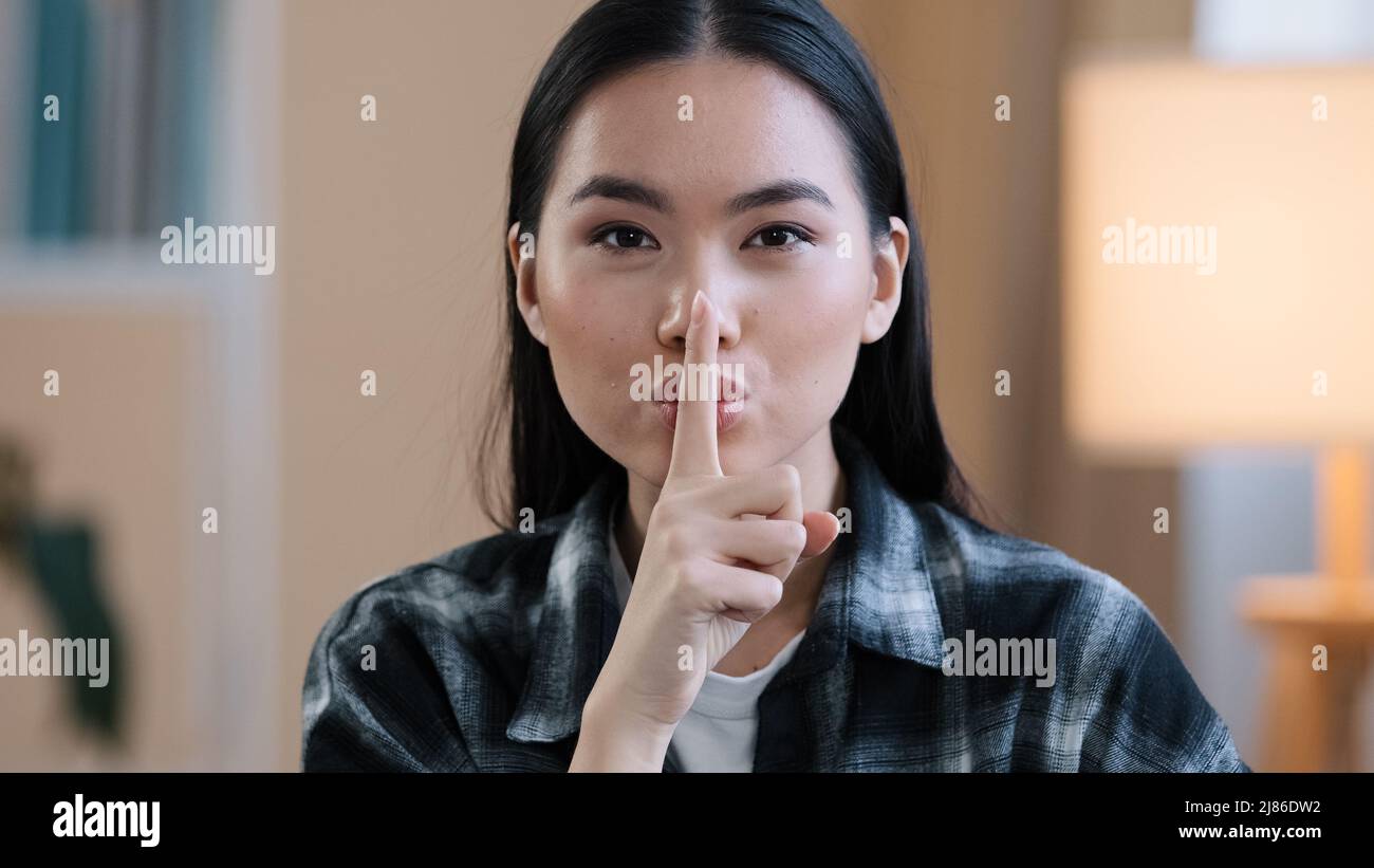 Portrait asian ethnic korean woman point with finger near mouth Chinese Japanese girl makes hush quiet gesture showing secret sign asks silent Stock Photo