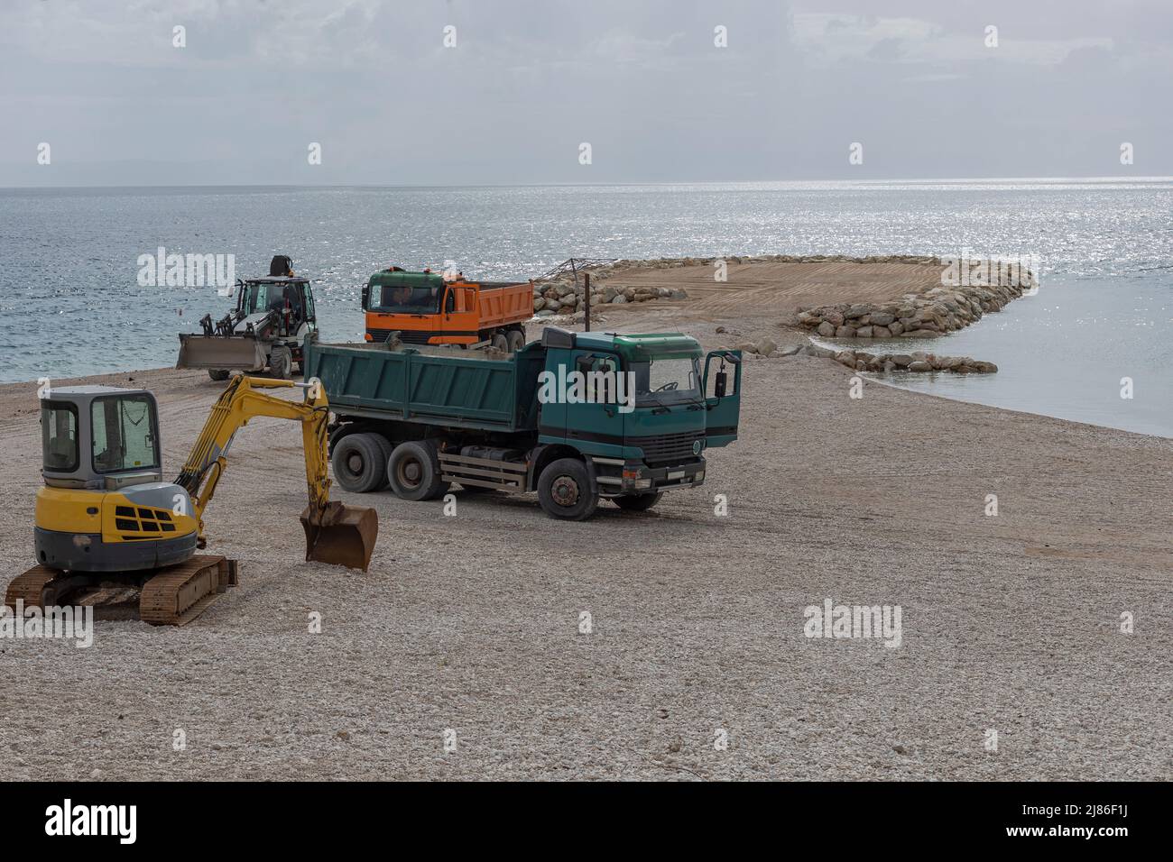 Plant vehicles including diggers and haulage trucks on a beach creating a beach which has been eroded by the sea Stock Photo