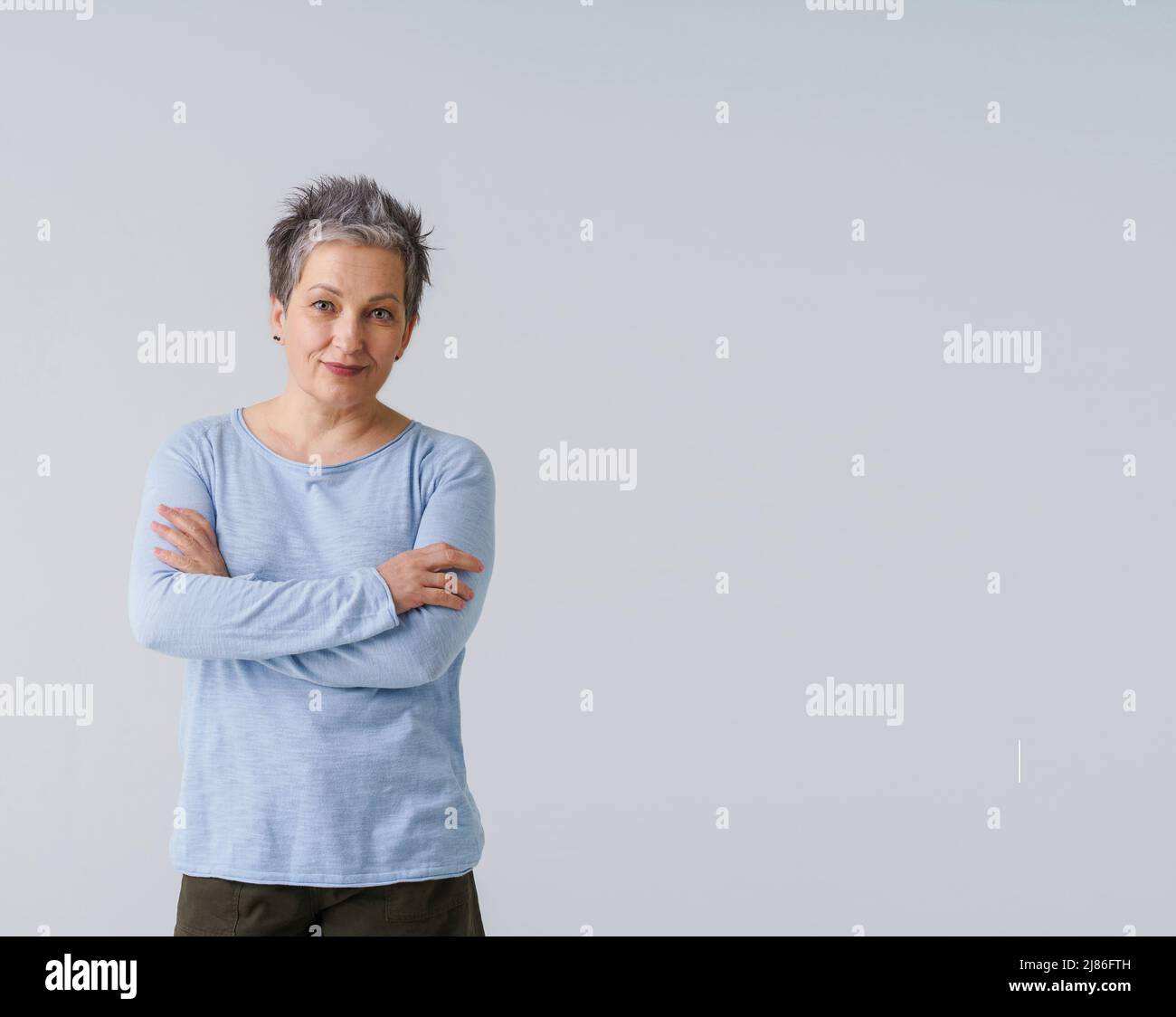 Challenging grey hair mature business woman in 50s posing with hands folded and copy space on right isolated on white background. Copy space and place for product placement. Aged beauty. Toned image. Stock Photo