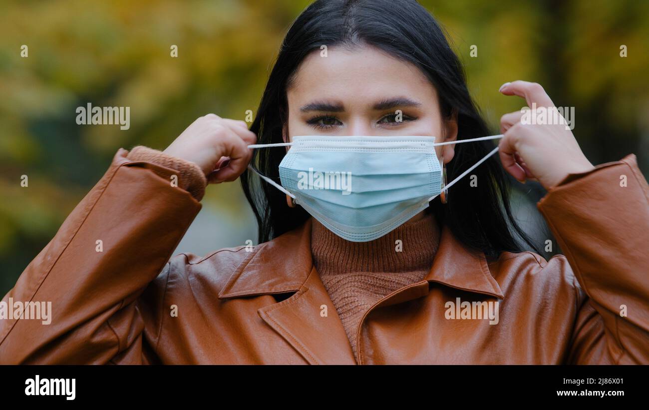 Close-up young woman stands outdoors in park takes off medical protective mask from face throw respirator smiling hispanic girl inhales deeply Fresh Stock Photo