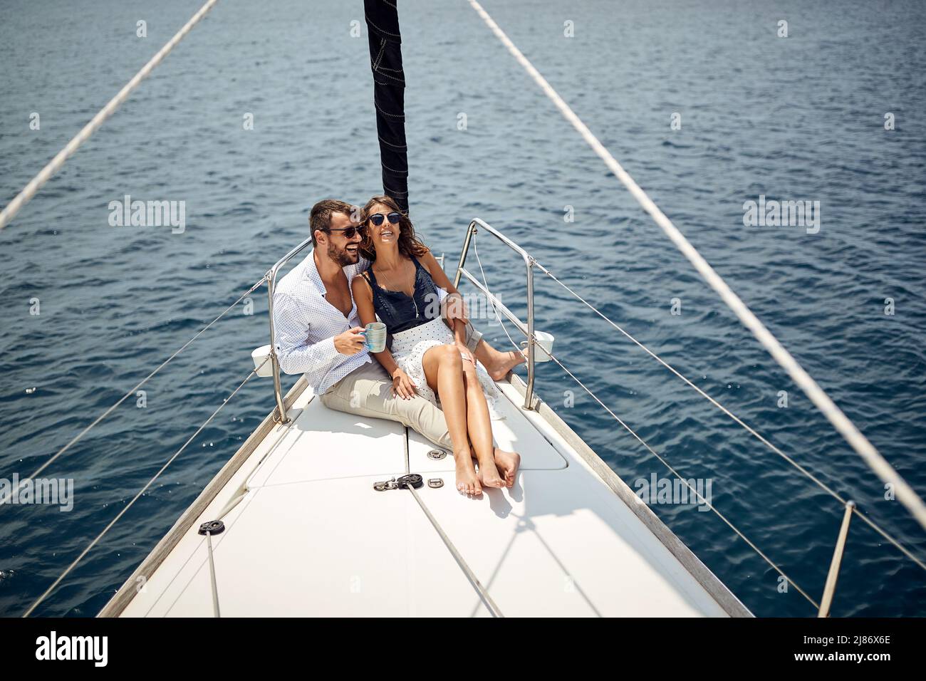 A young couple sitting on the bow of the yacht and enjoying a ride on a beautiful sunny day on the sea. Summer, sea, vacation, relationship Stock Photo