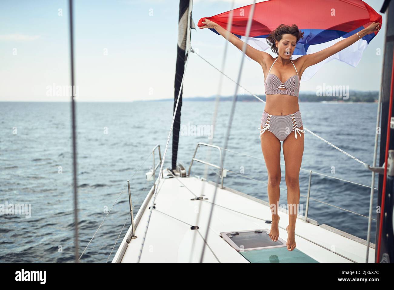 A young sexy girl is holding a flag and jumping while enjoying a ride on a beautiful sunny day on a yacht. Summer, sea, vacation Stock Photo