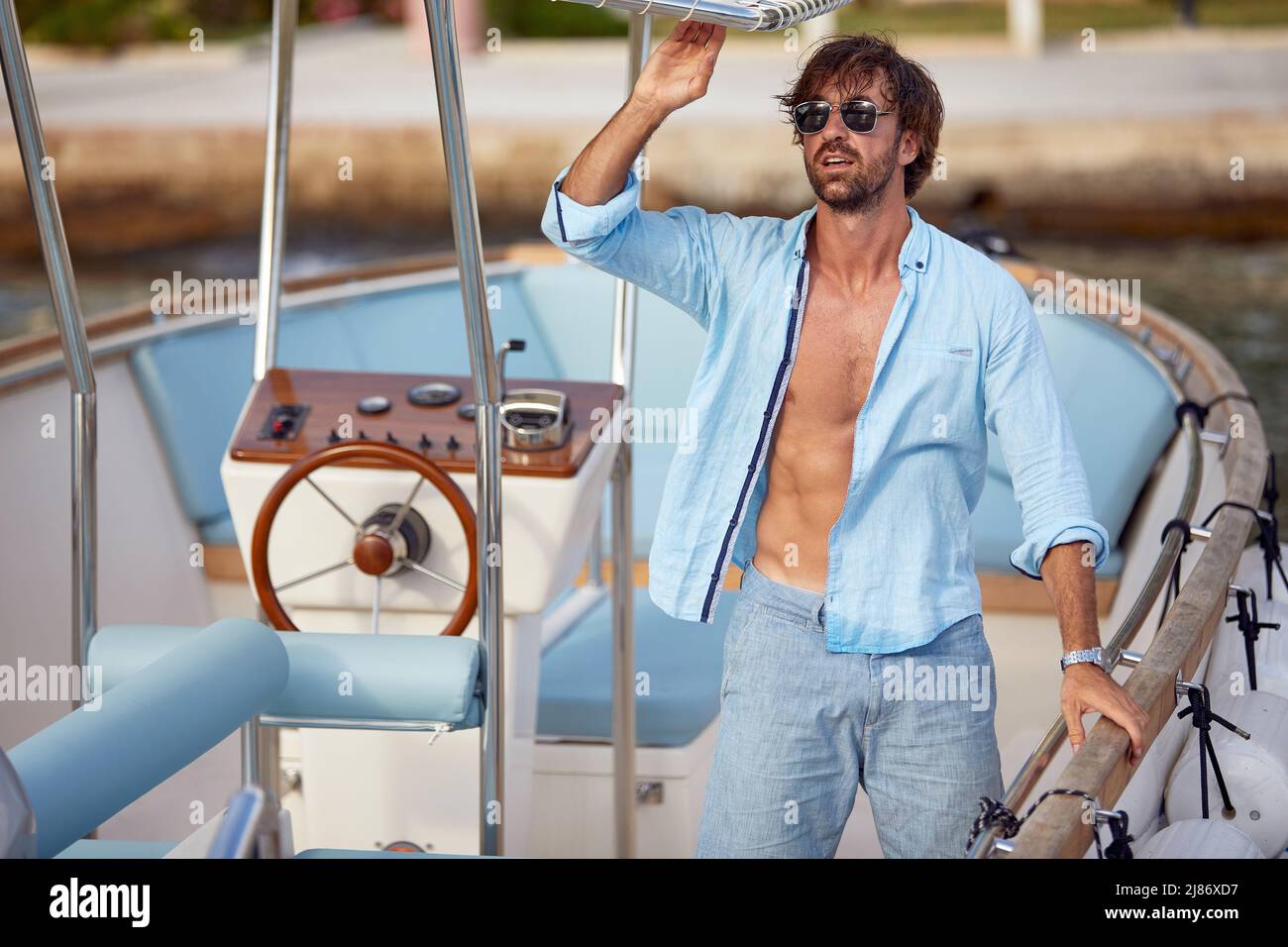 Handsome young man in sunglasses looking at sea on luxury yacht. Water sport vacation, summer outdoors. Holiday, leisure, lifestyle concept Stock Photo