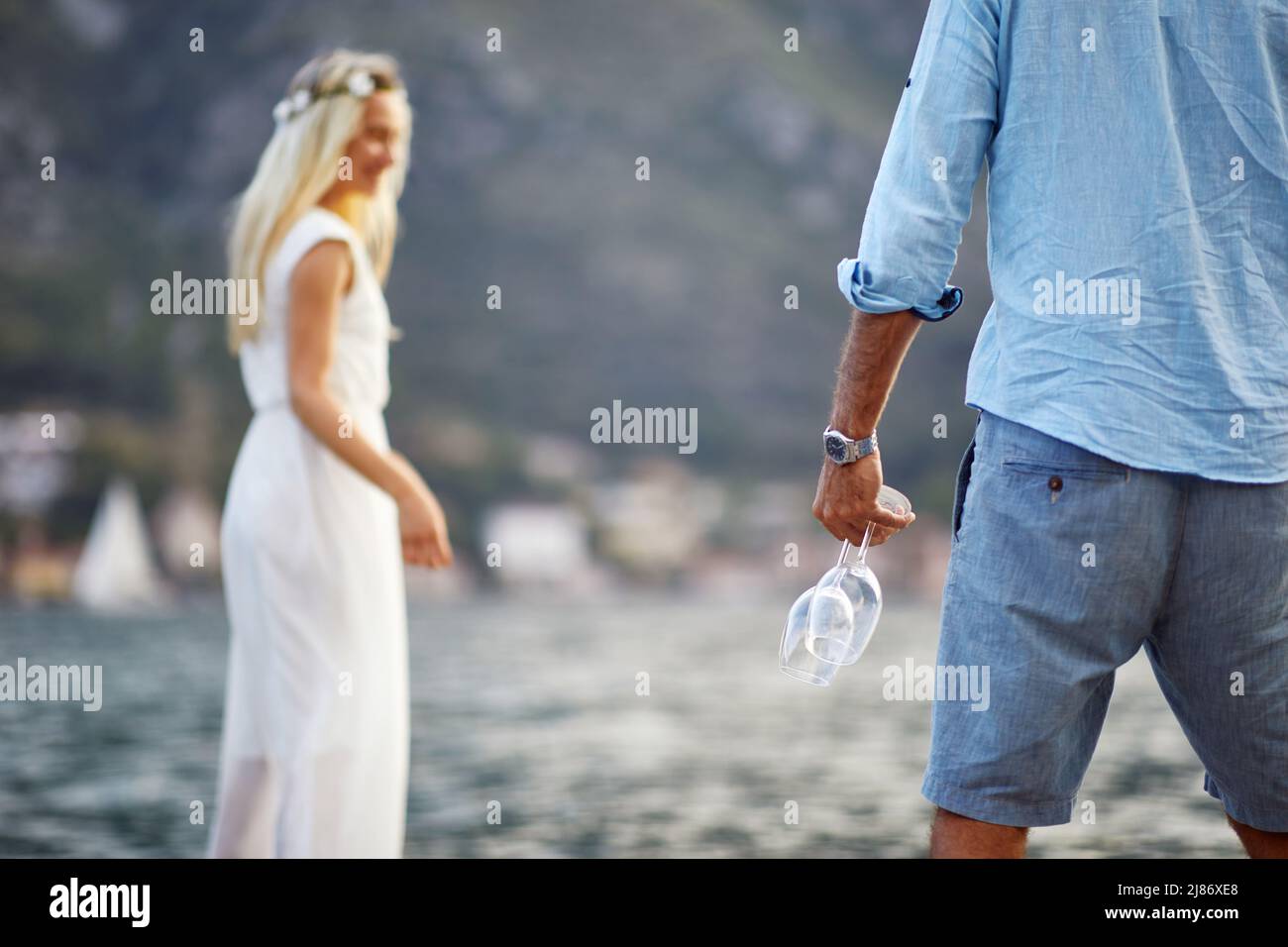 Romantic date by seaside, newlywed couple, bride in dress. Man with bottle of wine and glasses. Wedding, honeymoon, love concept Stock Photo