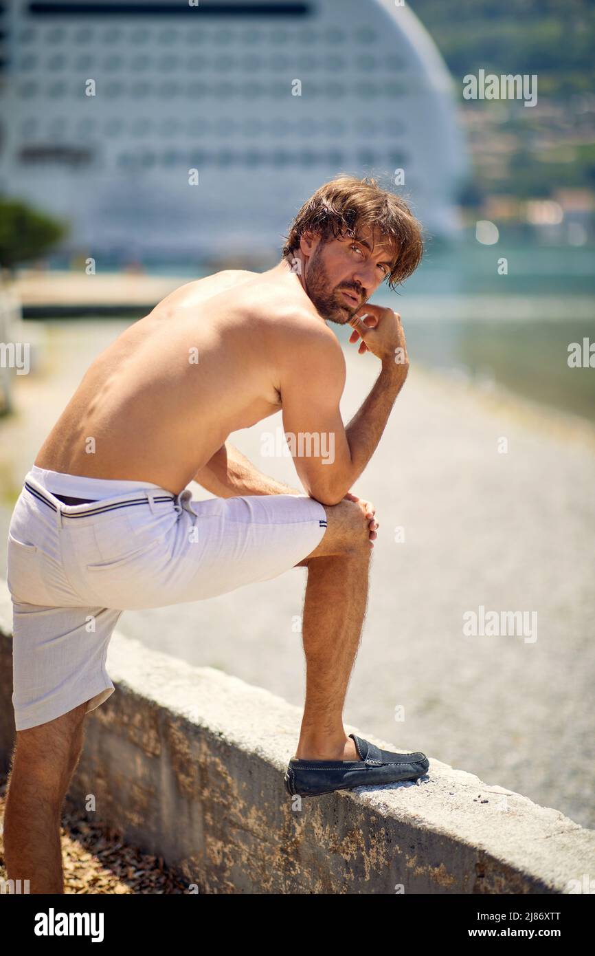 Handsome young athletic man posing on pier. Cruiser and sea in background. Lifestyle, sport, fashion, concept. Stock Photo