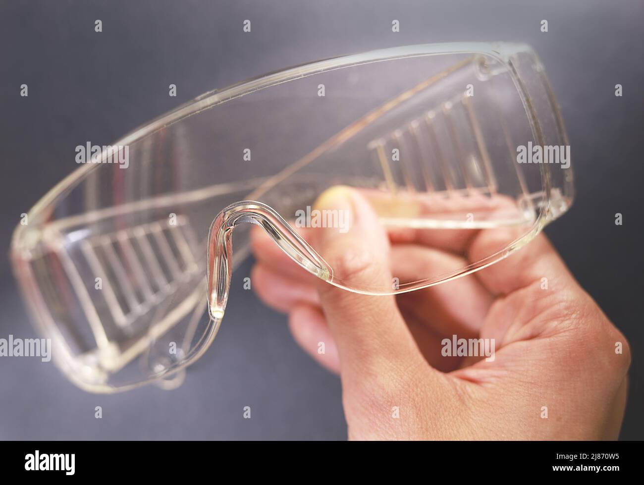 Protective glasses in hand, healthcare and safety concept. Safety glasses on black background. Personal protective equipment. Plastic goggles. Stock Photo