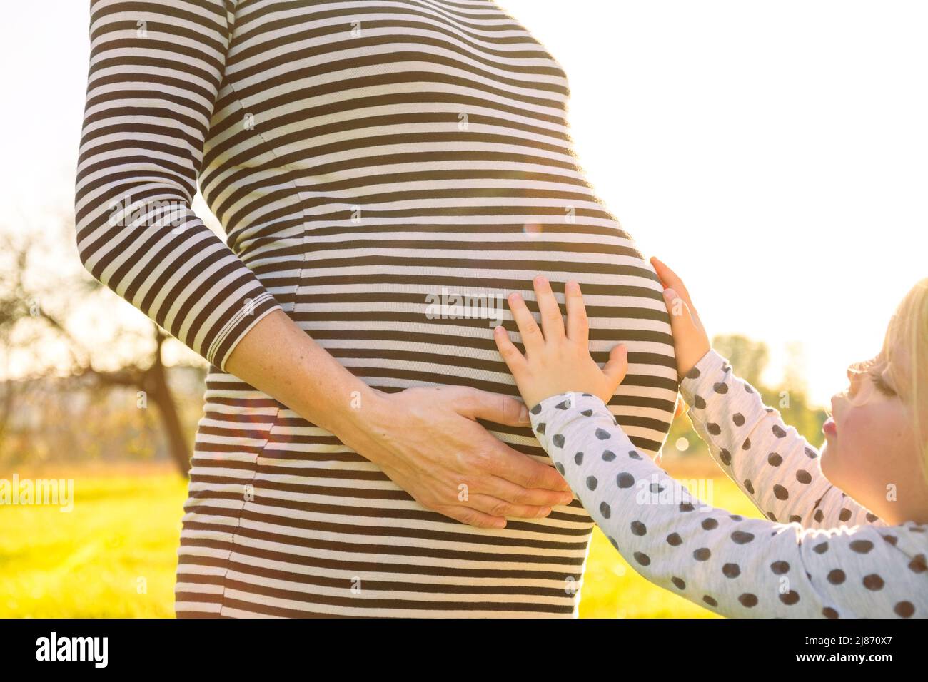 Young child touching the pregnant belly of her mother in beautiful evening sunlight Stock Photo