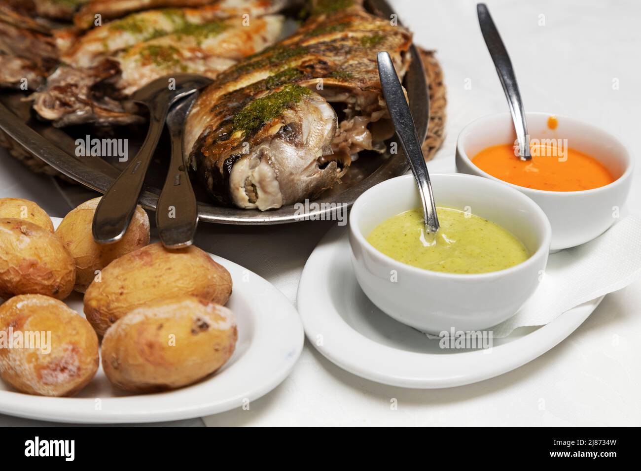 Wrinked potatoes (papas arrugadas) served with red sauce (mojo rojo) and green herby (mojo verde) plus a platter of grilled fish in Tenerife. The pota Stock Photo