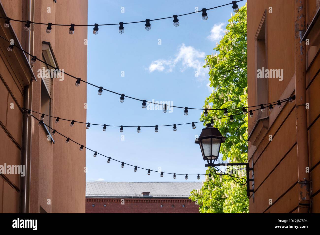 Light garland on the street at daylight. Decoration of the street with vintage Edison bulbs garland, festive city decorations Stock Photo