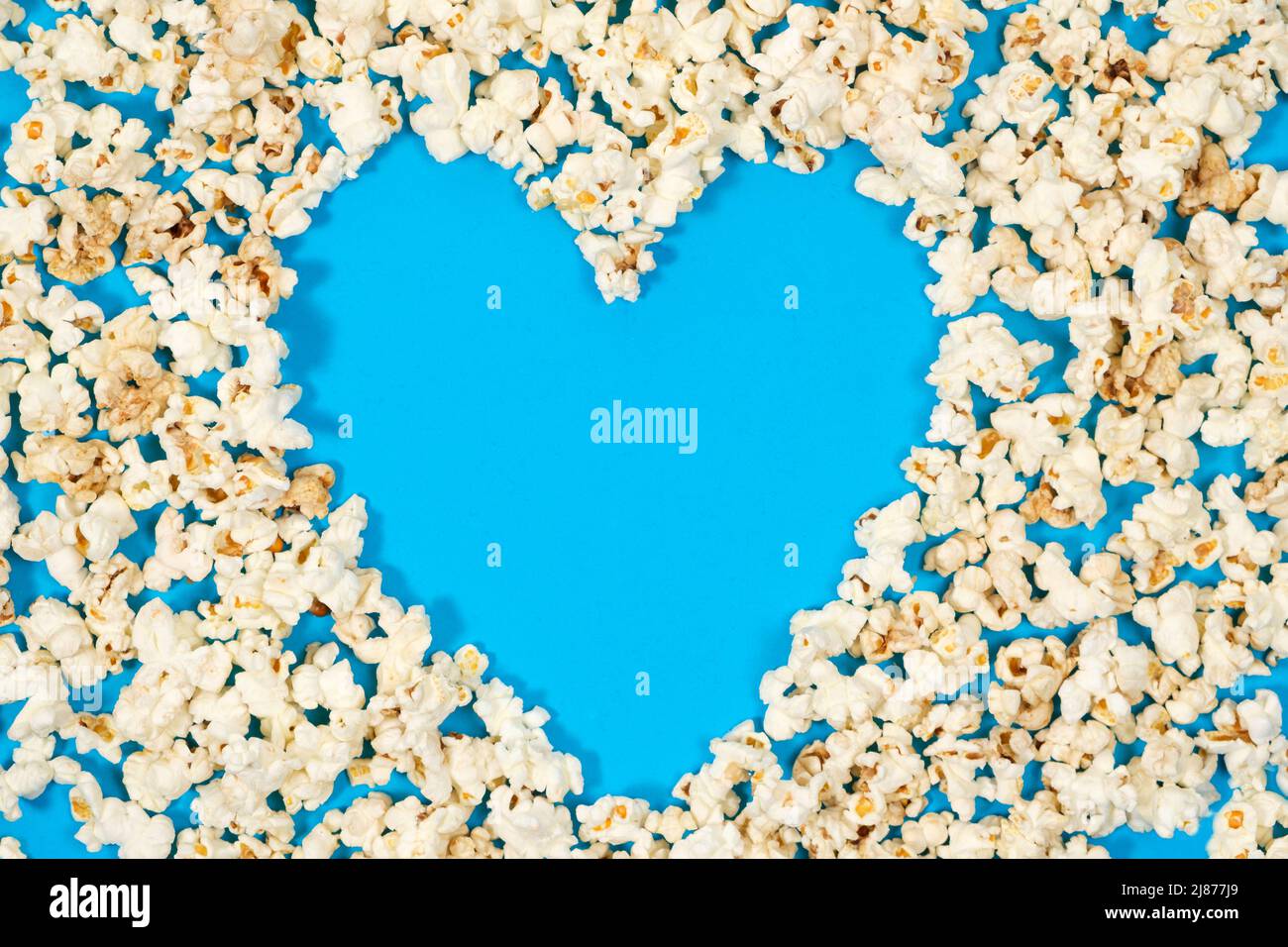 Popcorn is laid out in the form of a heart with a place for text on a blue background, top view. Stock Photo
