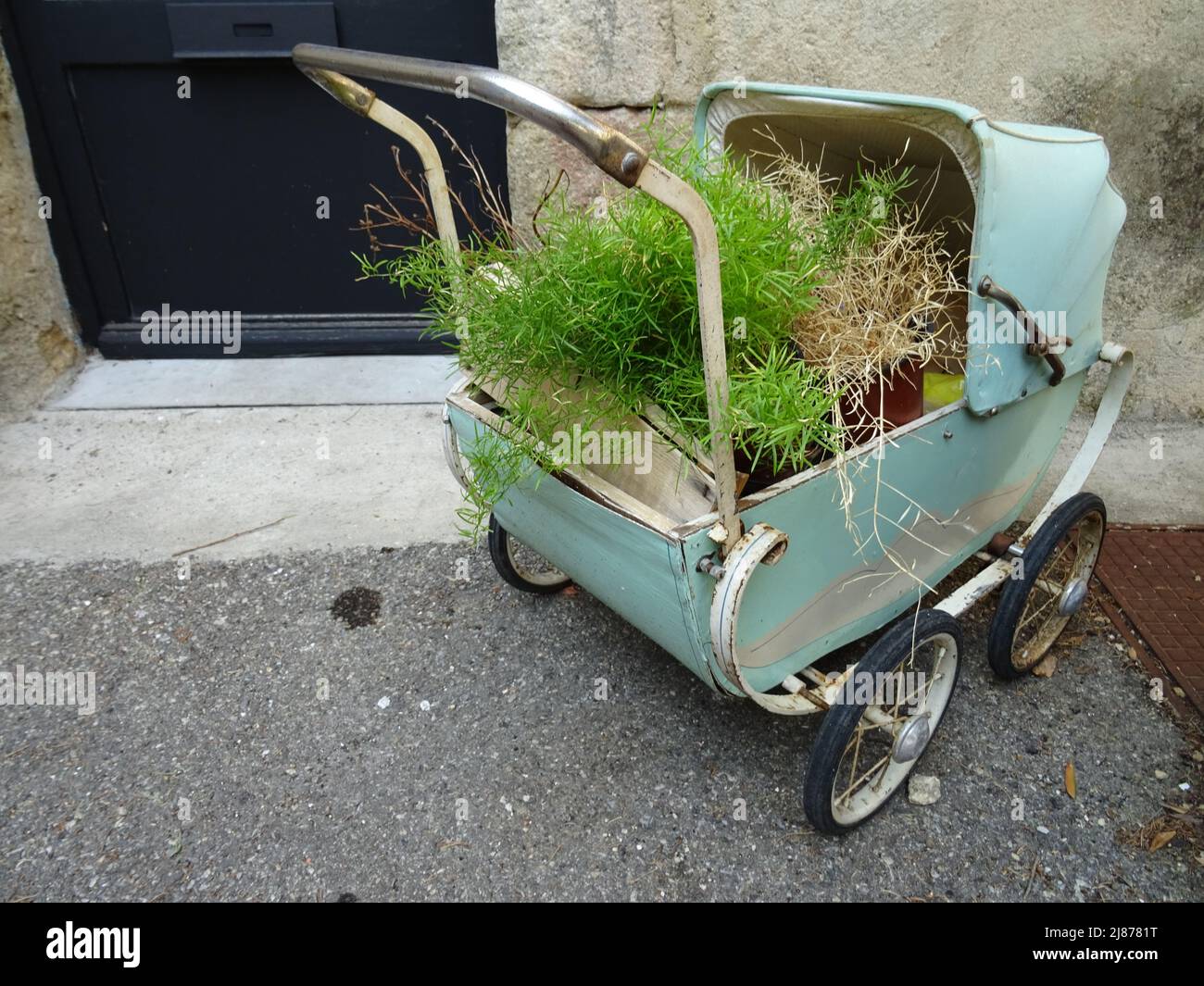 very old metal baby carriage as a flower bed in the street in france Stock Photo