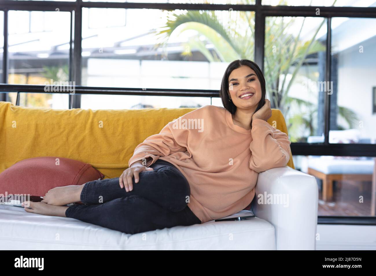 Portrait of beautiful smiling young asian woman wearing casuals while resting on couch at home Stock Photo