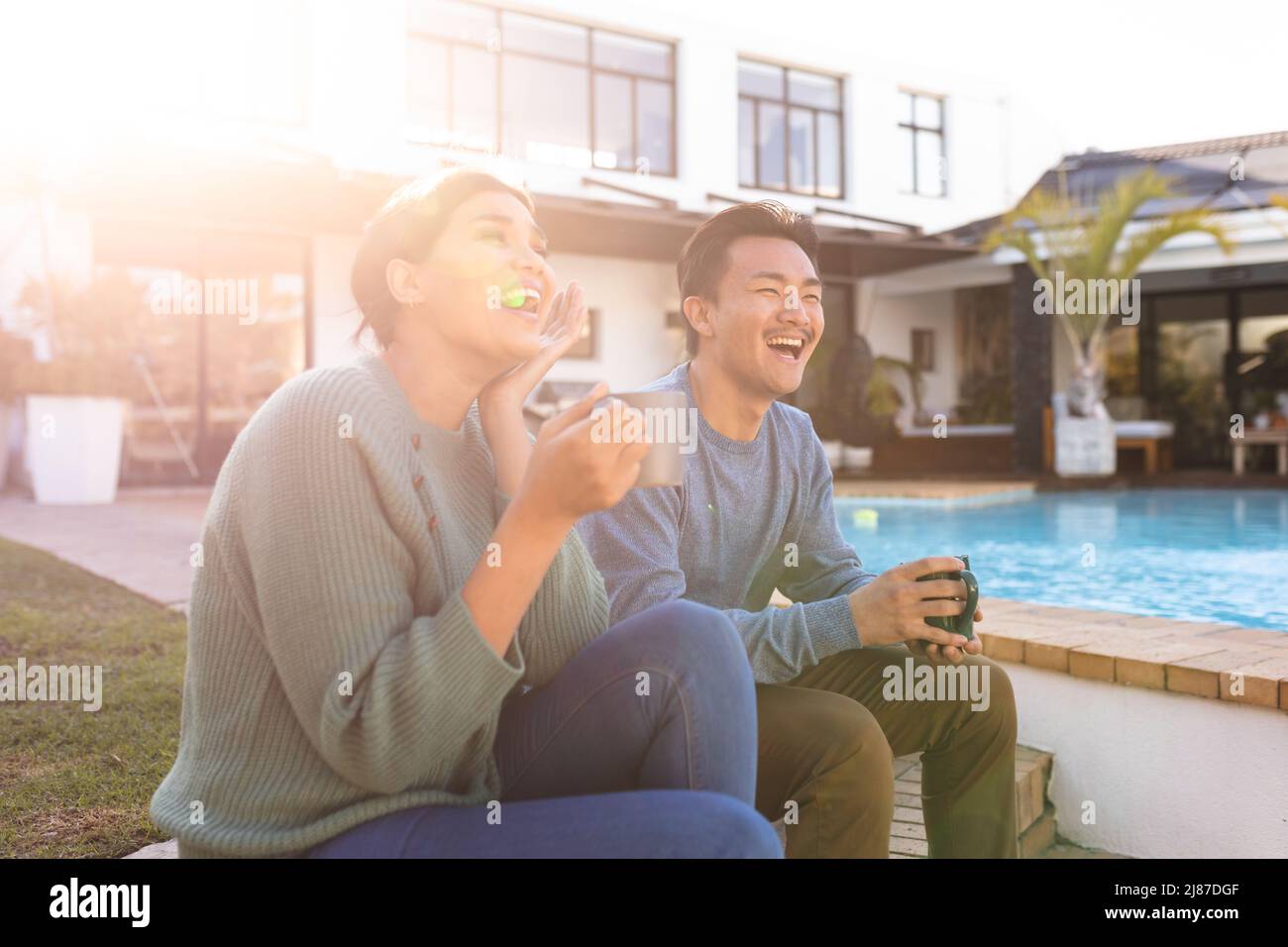 Cheerful young asian couple having coffee while relaxing outside house during sunny day Stock Photo