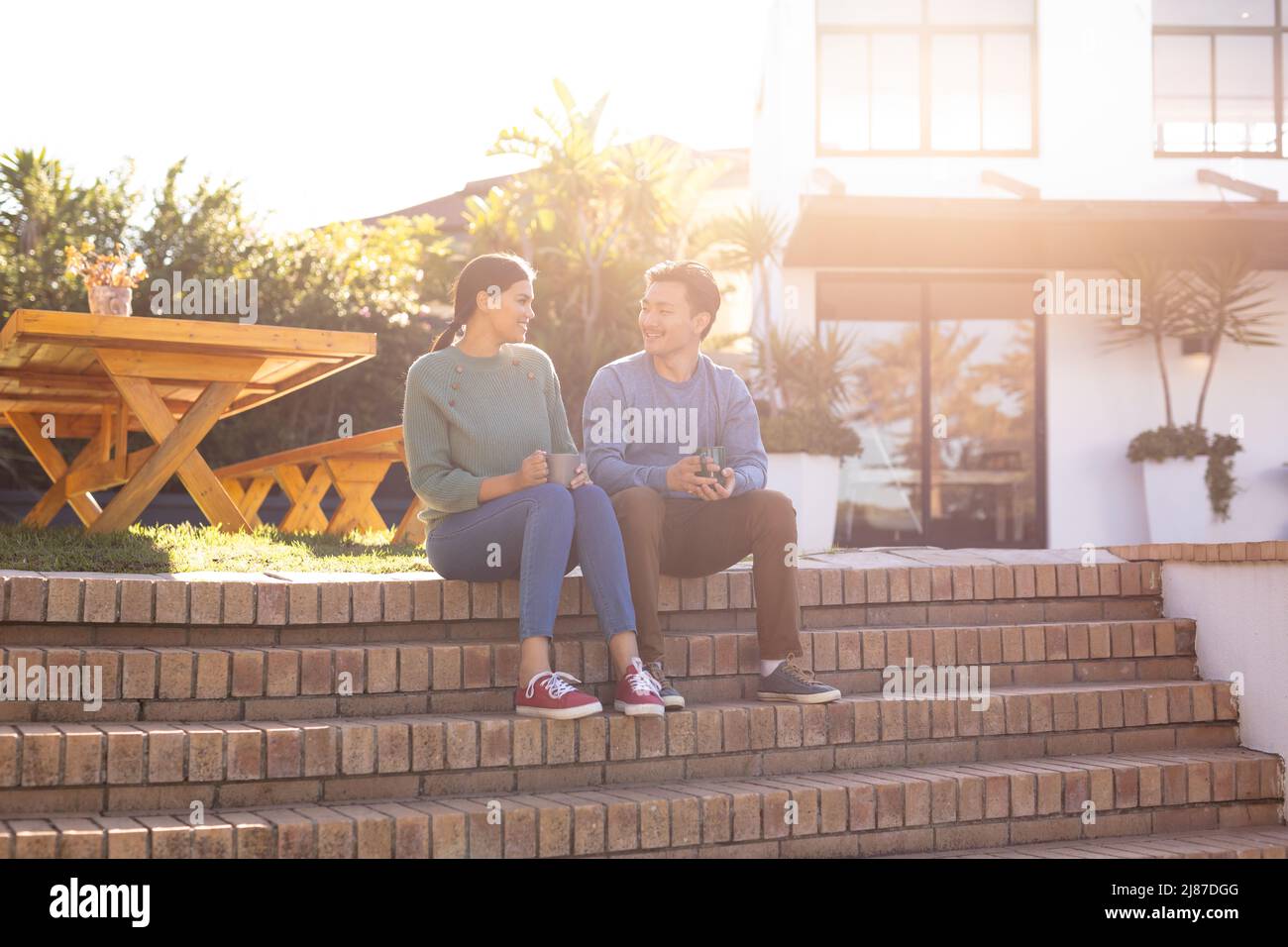 Loving young asian couple having coffee while sitting on steps outside house Stock Photo