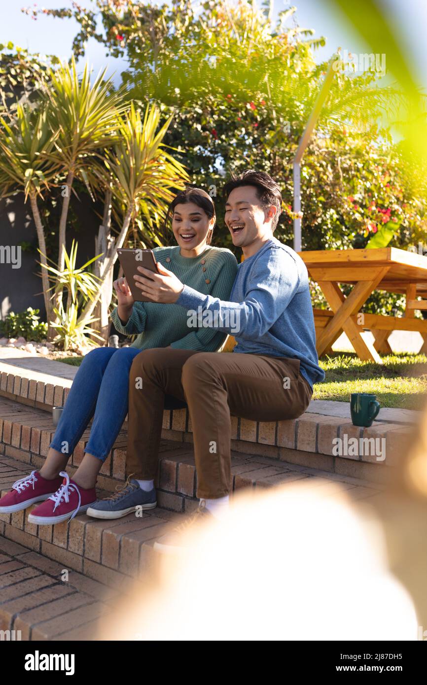 Cheerful asian young couple enjoying leisure time while looking at digital tablet in backyard Stock Photo