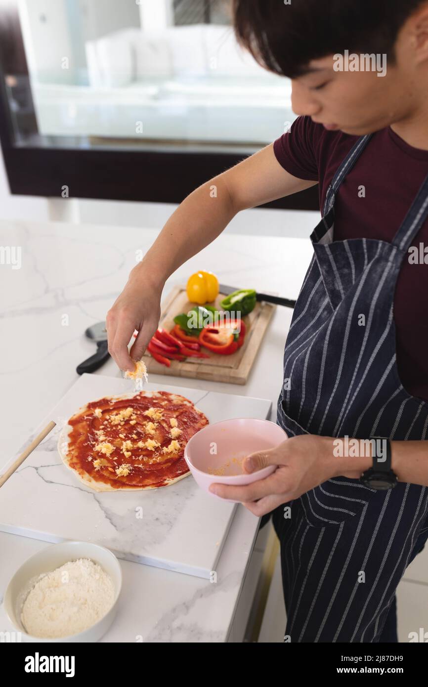 High angle view of asian teenage boy making pizza on kitchen island while standing at home Stock Photo