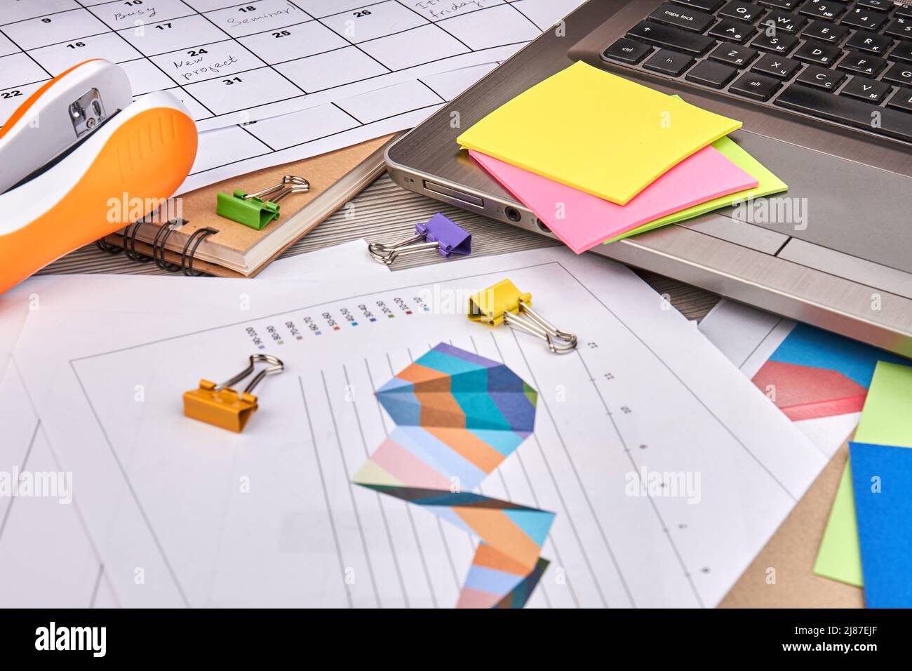 Work papers with charts and binder clips. Sticky notes with lapto and